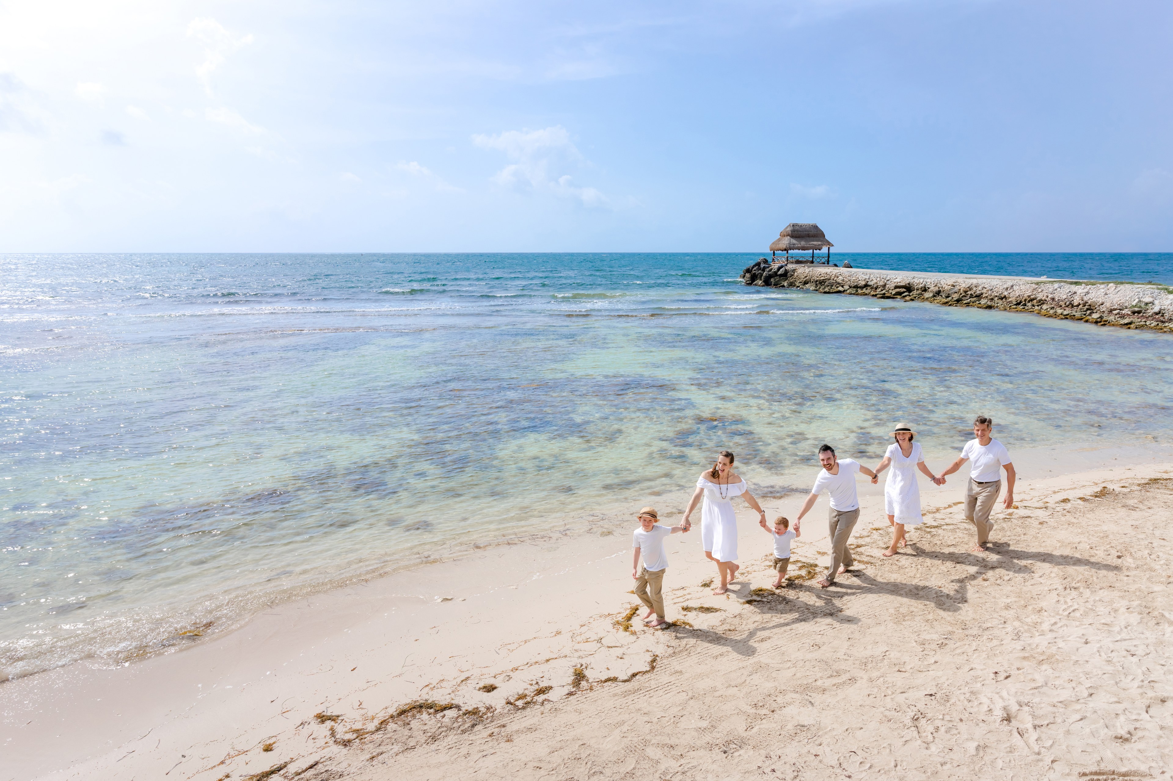 Three generations of a family with six children on Playa Delfines beach in Cancún at golden hour, the youngest seeing the ocean for the first time